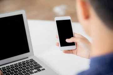 Hand of young man working with laptop computer and smartphone mockup on desk at home, notebook and phone display blank screen, freelance look message to internet, business and communication concept.
