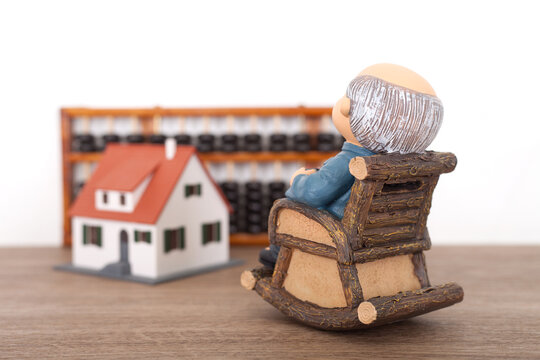 Grandpa sitting in a rocking chair looks at the model house and abacus tools in the distance