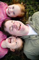 Father and Daughters Laughing Together While Lying in Grass Outside