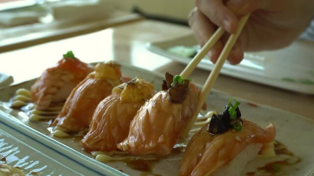 Chopsticks eating Japnese food aburi salmon nigiri with different sauces and topping