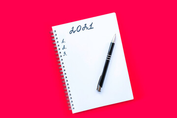 Notebook with a spiral and black pen on a red background. Planning list and numbers 1, 2 and 3. The inscription 2021. New Year and Christmas concept.