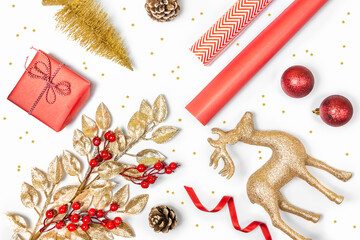 Christmas presents preparation - gift box, mistletoe, fircones,reindeer, christmas balls and paper in golden and red colors over white background.