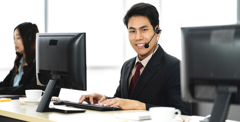 Group of happy asian smiling call center business operator customer support team phone services agen working and talking with headset on desktop computer at call center