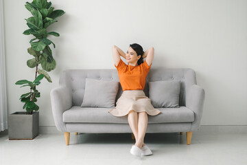 Peaceful young woman with hands behind head relaxing on cozy sofa at home