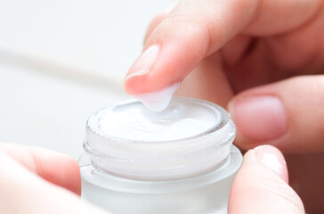 Hand of woman holding moisturizer cream and serum. She applying a facial cream , essential , oil , lotion and body cream for skin care, close up view and blur background. Beauty and Healthy Concept.