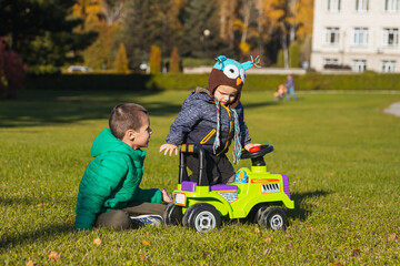 Two cheerful brothers-boys of different ages have fun playing with a big jeep in a wheelchair on a green field on a warm summer day. Brothers friendship and happy childhood concept.