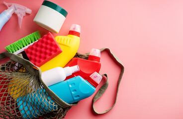 sanitary bottles and cleaning tools in mesh bag on pink background with copy space