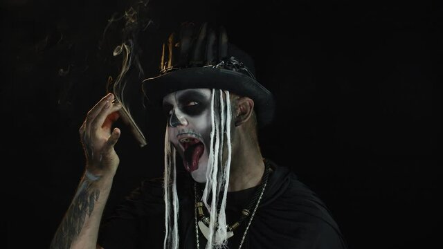 Scary guy in carnival costume of Halloween skeleton smoking cigar, making faces, showing tongue