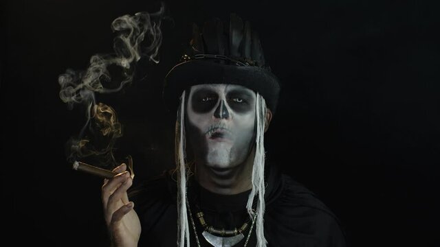 Creepy man with skeleton makeup in top-hat. Guy smoking cigar, opening his eyes, making faces