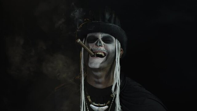 Frightening man in skeleton Halloween cosplay costume smoking cigar, smiling, laughing. Slow motion