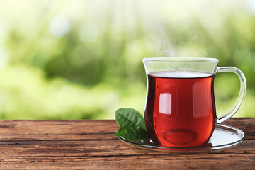 Glass cup of fresh hot tea on wooden table against blurred green background. Space for text