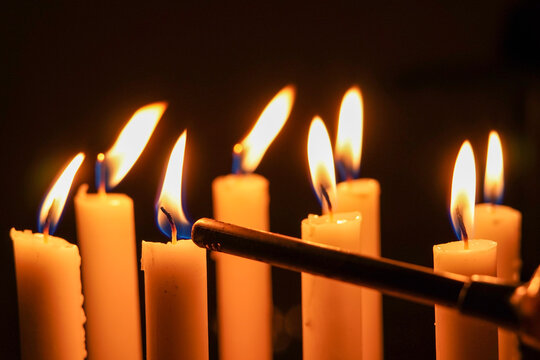 Close up photo of a candlelight being ignited using a portable fire igniter, close up of burning candles in the dark.