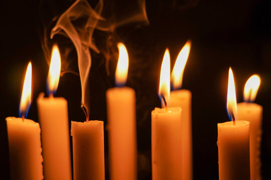 Close up photo of group candlelight in the dark with one of them dies out and smoke comes out of it, close up of burning candles in the dark.