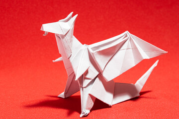 white origami dragon made with white paper in a red background with hard shadows