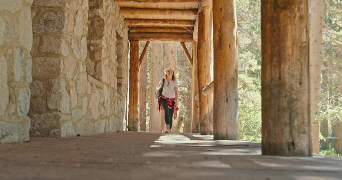Hiker woman walking by deck of stone hunting house in the woods. Attractive woman with hiking backpack enjoying sunny day in the green forest. 4K slow motion outdoor adventure and wild nature travel 