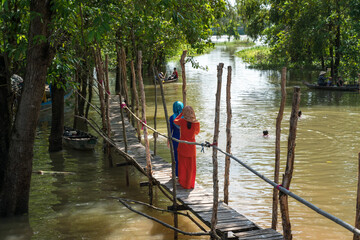 Wooden bridge in floating water season in Mekong delta, southern Vietnam, with Muslim girls walking on the bridge