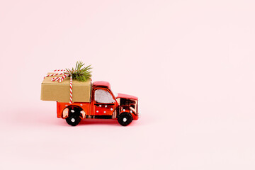 Red toy car delivering Christmas or New Year gift present box on pink background.
