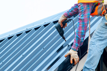 Roofer with electric drill used on new roofs with Metal Sheet on top roof at the building under construction. © visoot