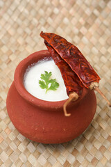 Bowl of homemade sour cream/curd/yogurt with fresh herbs in clay pot on a mat, Kerala, India. Dairy...