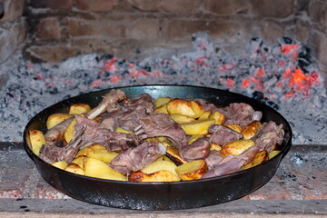 Delicious grilled meat with potatoes in pan on open flame