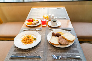 Fresh romantic breakfast table next to morning briliant light window, with bread, pastry, spaghetti, fruit, juice