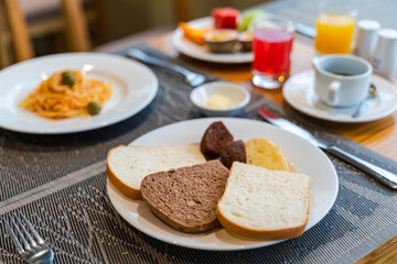 Fresh romantic breakfast table next to morning briliant light window, with bread, pastry, spaghetti, fruit, juice, coffee cup