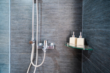 Hotel bathroom closeup with stainless hanging shower, bottles of shower and shampoo gel