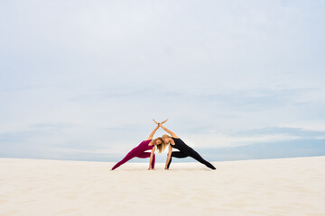 Two beautiful young women performing yoga pose parshvakonasana together on the beach