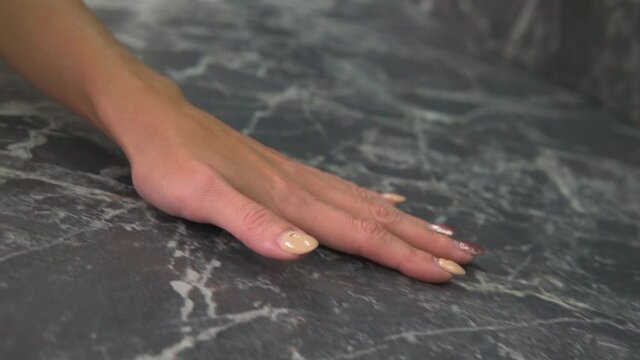 Woman hand is touching dark granite kitchen countertop. Slow motion tracking close-up shot.