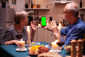 Elderly man and woman waving at phone with green screen. Aged people looking at mockup template...