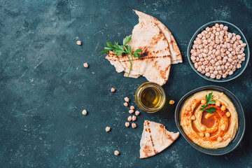 Hummus, chickpea dip, olive oil, raw beans, smoked paprika, pita on dark authentic background....