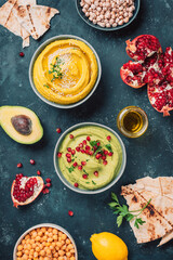 Ingredients for yellow hummus and green hummus - chickpea, tahini, olive oil, sesame seeds, pita, avocado, pomegranate on dark background. Middle eastern, jewish, arabic cuisine. Top view. Copy space
