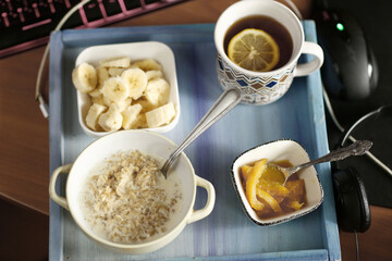 healthy breakfast on blue tray - porridge, cut banana, orange jam, lemon tea with spoon and tea strainer