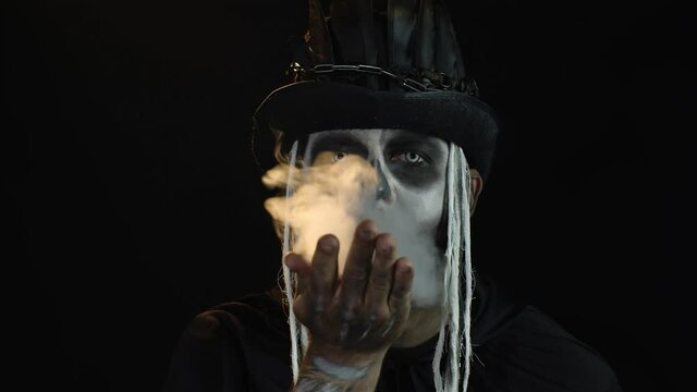 Sinister man with horrible Halloween skeleton makeup making fly air kiss with smoke. Day of The Dead