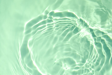 De-focused closeup of mint green transparent clear calm water surface texture with splashes and bubbles. Trendy abstract summer nature background. Mint colored waves in sunlight with copy space.