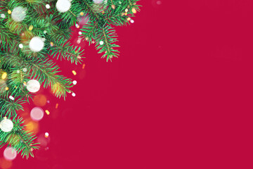 Festive composition with border of fluffy dark green fir branches and gold Christmas lights bokeh on red background. Top view, flat lay style, copy space for text.