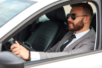 Fototapeta na wymiar cool businessman in black sunglasses sits inside of car, drive it. successful male in formalwear, in suit.