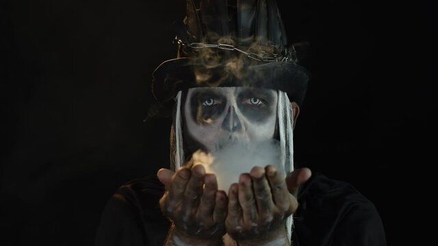 Scary man in thematic carnival costume of Halloween skeleton making fly air kiss with smoke
