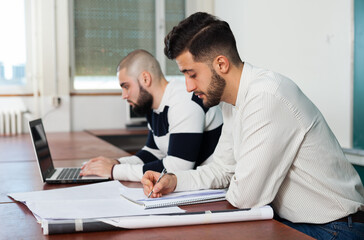 Obraz premium Two male university students sitting at desk preparing for exams together in classroom