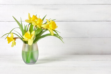 yellow daffodils at glass vase on bright wood table on white background