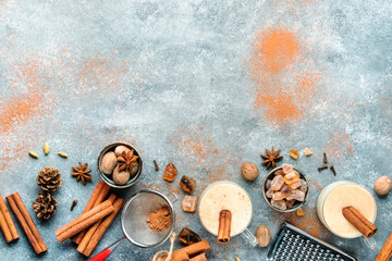 Eggnog hot winter or autumn cocktail drink with milk, eggs and dark rum, sprinkled with cinnamon and nutmeg in glass cups on gray background, Christmas table setting, top view