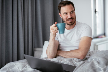 Young man watching movie in bed. Handsome man enjoying in morning..