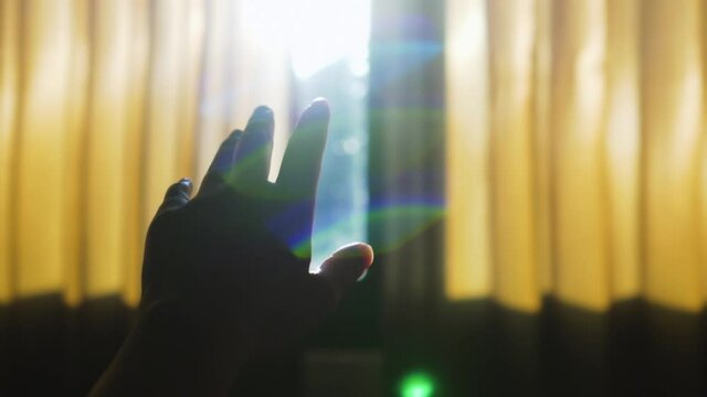 Slow motion, asian woman's hand reaching the sunlight, she looks at the sun through her hand in the bedroom. The sun shine through the hand.
