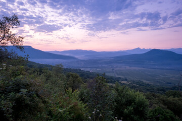 Early morning one hour before dawn. Silhouettes of mountains in the morning haze, grass and trees in the foreground. Lagonaki Plateau, Republic of Adygea, Russia