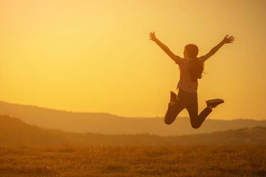 Happy teenage girl jumping in nature in sunset.