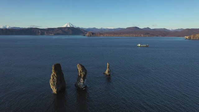 Autumn scenery, beautiful sunrise over Avacha Bay on Russia's Kamchatka Peninsula, and the famous Three Brothers Rock. The waters of the Pacific Ocean. In the background is the Avachinsky volcano.