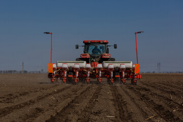 Obraz premium Tractor with sowing machine working on a field. Seeding - sowing crops at agricultural fields in spring.