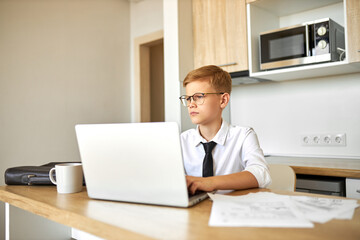 little caucasian boy work on laptop at home, young office worker in formal wear is concentrated on online work, during quarantine. children pretend to be adults