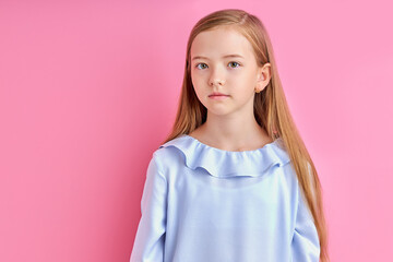 Fototapeta premium calm little girl with natural long hair look at camera, wearing blue blouse, posing, isolated on pink background
