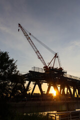 Fototapeta na wymiar 建築中の鉄橋と夕日と巨大なクレーン